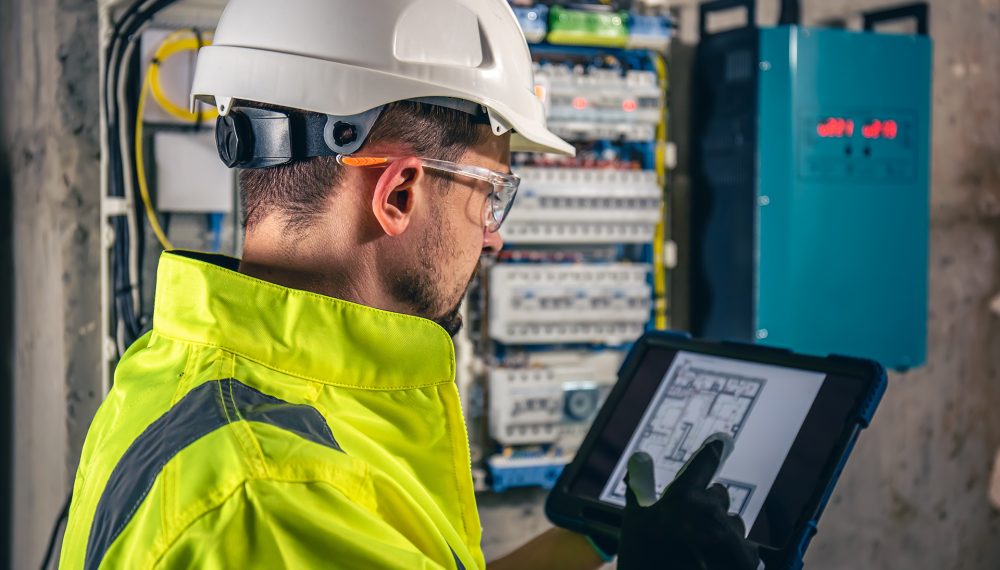 Man, an electrical technician working in a switchboard with fuses. Installation and connection of electrical equipment. Professional uses a tablet.